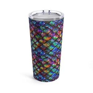 May include: A stainless steel travel tumbler with a colorful, iridescent scale pattern in shades of blue, green, purple, and gold. The tumbler has a silver rim and a clear lid. The design resembles a mermaid or dragon scale pattern.