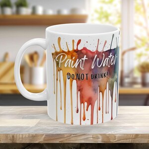 May include: White ceramic mug with a colorful watercolor design of paint dripping down the side. The text "Paint Water Do Not Drink!" is printed on the mug.