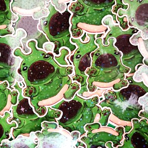 May include: A collection of green stickers featuring a cartoonish creature with large eyes, a brown nose, and star-like accents. The stickers have a white border and a glittery effect, creating a playful and whimsical design.