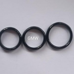 Könnte beinhalten: Drei schwarze Ringe, jeder mit einer glatten, polierten Oberfläche. Die Ringe sind in einer Reihe angeordnet, wobei der mittlere Ring etwas größer ist als die beiden anderen.