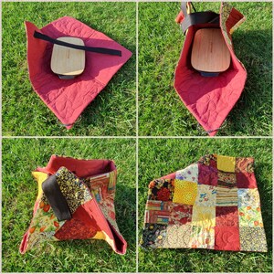 May include: Four different views of a red quilted fabric storage bag with a black strap. The bag is folded flat, open, and closed. The bag is made of patchwork fabric with a variety of colours and patterns.