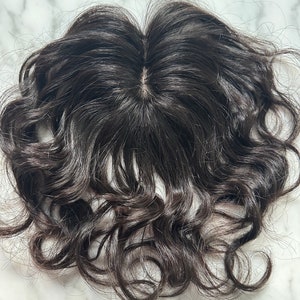 May include: Dark brown, curly hair topper with a natural-looking part. The hairpiece appears to be made of human hair, with a wavy texture and a dark, rich color. The hair is styled in loose curls.