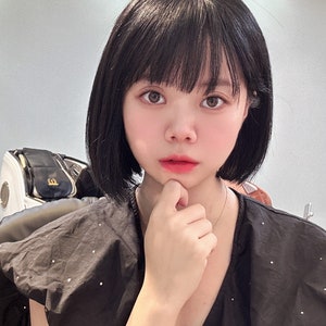 以下が含まれることがあります： 黒髪で前髪のある女性が、白のドット柄の黒いシャツを着ています。彼女は赤いハートのチャームが付いた金のブレスレットをしています。