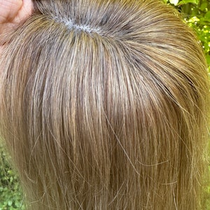 Puede incluir: Un topper de cabello humano castaño claro con una base fina y transparente. El cabello es liso y parece tener unos 30 cm de largo.