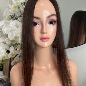 Può includere: Un topper di capelli umani di colore marrone scuro con capelli lunghi e lisci. Il topper è su una testa di manichino.