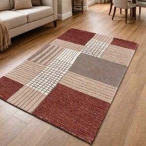 May include: A rectangular area rug with a geometric pattern in shades of red, beige, and brown. The rug features squares, rectangles, and striped sections, creating a modern design. The rug is placed on a hardwood floor.