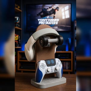 Pode incluir: Um conjunto de acessórios para jogos com um suporte em forma de skate marrom, fones de ouvido brancos e cinza e um controle de jogo branco e azul. O suporte segura os fones de ouvido e o controle, com uma TV exibindo "Tony Hawk's Pro Skater II" ao fundo.