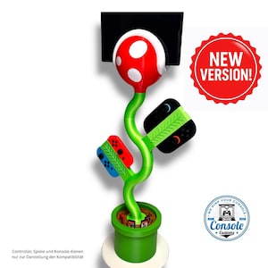 Könnte beinhalten: Ein grüner, roter und weißer Videospiel-Controller-Halter in Form einer Piranha-Pflanze. Der Halter hat Schlitze für Gamecontroller und einen Sockel, der einer grünen Röhre ähnelt. Ein roter Aufkleber lautet "NEW VERSION!"