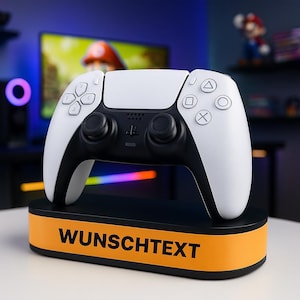 Può includere: Un controller PlayStation 5 bianco e nero appoggiato su un supporto nero con una fascia arancione. Il supporto presenta la scritta "WUNSCHTEXT". Il controller ha il layout standard dei pulsanti e due joystick neri.