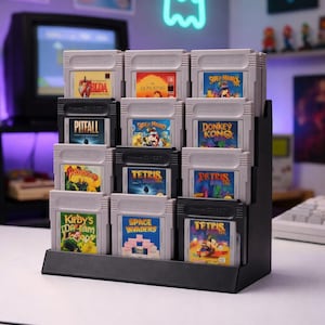 Può includere: Un espositore nero per cartucce di giochi per Game Boy pieno di varie cartucce. Le cartucce presentano titoli come "Zelda", "Lion King", "Super Mario", "Pitfall", "Donkey Kong", "Tetris", "Kirby's Dream Land" e "Space Invaders".