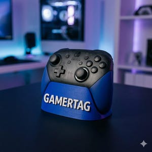 May include: A black and blue gaming controller with the word "GAMERTAG" in white lettering on a blue base. The controller has multiple buttons and a joystick. The background is blurred.