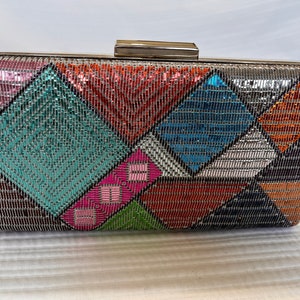 May include: A silver clutch purse with a geometric pattern of colorful sequins. The sequins are arranged in a diamond pattern and are in shades of pink, blue, green, orange, and silver.