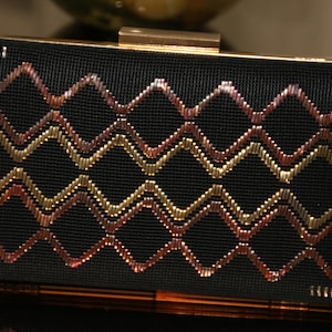 May include: A black clutch purse with a gold clasp and a geometric pattern of gold and copper thread embroidery.