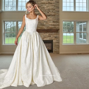 May include: Ivory wedding gown with a floral pattern, featuring a fitted bodice and a full skirt. The dress has a scoop neckline and wide straps. The brand name "Blissfullbrides" is visible on the skirt.