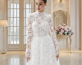 Può includere: Un abito da sposa in pizzo bianco con maniche lunghe e collo alto. L'abito presenta dettagli floreali in pizzo e un corpetto aderente. La gonna arriva fino a terra. L'abito è indossato in una stanza luminosa con uno specchio e fiori sullo sfondo.