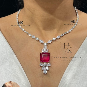 Pode incluir: Um colar prateado com um grande pingente quadrado de pedra rosa. O pingente é rodeado por pedras preciosas claras menores. O colar tem um design correspondente com pedras preciosas claras. O texto "HK PREMIUM QUALITY" é visível.