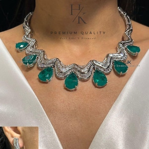 May include: A luxurious necklace and earring set featuring emerald green teardrop-shaped gemstones. The necklace has a wavy design with baguette-cut diamonds and emeralds. The earrings mirror the necklace's design. The text "PREMIUM QUALITY" is visible.