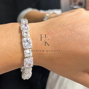 Puede incluir: Un brazalete plateado con piedras grandes, cuadradas y transparentes, dispuestas en fila. El brazalete está en una muñeca, con un segundo brazalete visible en el fondo. La imagen incluye el texto "HK PREMIUM QUALITY Feel Like a Diamond."