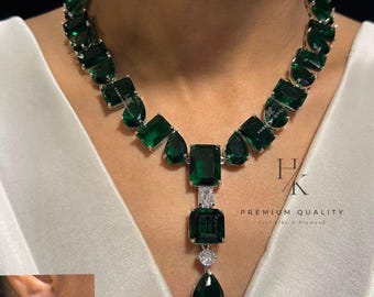 May include: A necklace and earring set featuring emerald-green rectangular, pear, and square-cut gemstones. The necklace has a pendant with a large emerald-green stone and a smaller white stone. The earrings mirror the pendant design. The text "PREMIUM QUALITY" is visible.