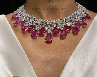 May include: A dazzling necklace and earring set featuring a silver-toned metal base adorned with clear, sparkling crystals and vibrant, teardrop-shaped ruby-red gemstones. The necklace drapes elegantly, complemented by matching earrings. The image includes the text "PREMIUM QUALITY Feel Like A Diamond".