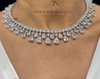 May include: A dazzling white necklace with teardrop-shaped pendants and matching earrings. The necklace features multiple rows of sparkling stones, with the text "PREMIUM QUALITY" and "Feel Like A Diamond" visible. The product code is N-1559-WHITE.