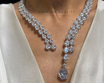 May include: A dazzling silver necklace and matching earrings set. The necklace features a cascading design of clear, sparkling stones, with a large teardrop pendant. The earrings mirror the necklace's design. The image includes the text "PREMIUM QUALITY Feel Like a Diamond."