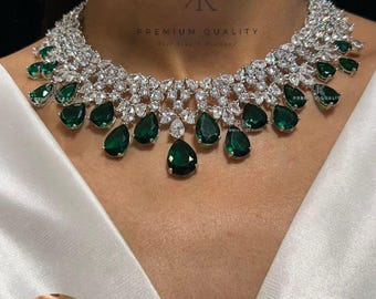 May include: A silver necklace with a teardrop design features green and clear stones. Matching earrings with a similar design are shown in a smaller image.