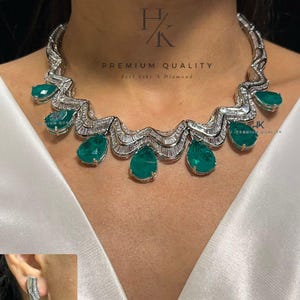 May include: A silver necklace with a wave-like design and emerald green stones. The necklace is paired with matching earrings. The text "PREMIUM QUALITY Feel Like A Diamond" is visible on the image.