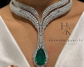 May include: A dazzling silver-toned necklace and matching earring set. The necklace features a layered design with a large, pear-shaped emerald-green gemstone pendant. The earrings mirror the pendant's design. The image includes the text "PREMIUM QUALITY Feel Like A Diamond".