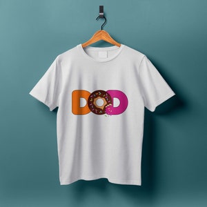 K&ouml;nnte beinhalten: Wei&szlig;es T-Shirt mit dem Wort "DONUT" in orangefarbenen und rosafarbenen Buchstaben. Das "O" in "DONUT" ist ein Schokoladen-Donut mit rosa Zuckerguss und Streuseln.