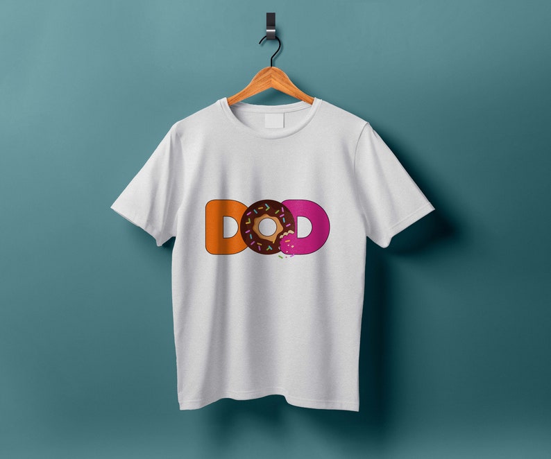 K&ouml;nnte beinhalten: Wei&szlig;es T-Shirt mit dem Wort "DONUT" in orangefarbenen und rosafarbenen Buchstaben. Das "O" in "DONUT" ist ein Schokoladen-Donut mit rosa Zuckerguss und Streuseln.