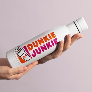 K&ouml;nnte beinhalten: Eine wei&szlig;e Edelstahl-Wasserflasche mit einem pinkfarbenen und orangen Dunkin' Donuts-Logo, auf dem "Dunkie Junkie" steht, und einer stilisierten Kaffeetasse mit den Buchstaben "DJ".