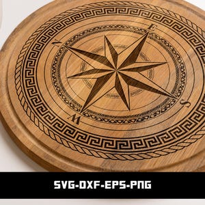 May include: A circular wooden chopping board with a compass design etched into the surface. The compass rose features directional indicators and a starburst design. The board has a Greek key border and a rope-like edge. The text "SVG-DXF-EPS-PNG" is at the bottom.