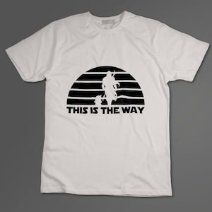 May include: White t-shirt with a black silhouette of a Mandalorian and Grogu walking in front of a sunset with the text "This is the Way".