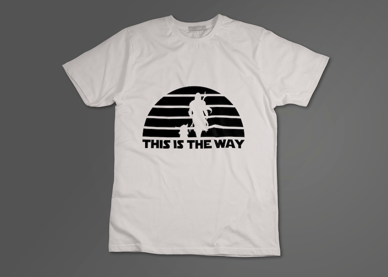 May include: White t-shirt with a black silhouette of a Mandalorian and Grogu walking in front of a sunset with the text "This is the Way".