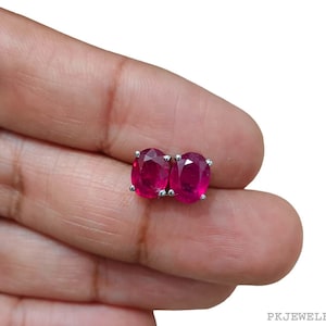 Pode incluir: Um par de brincos de rubi de forma oval, engastados em prata. Os brincos são de cor vermelha intensa e têm um acabamento polido.
