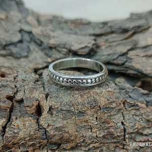 Peut inclure: Une bague en argent avec un motif de perles. La bague est sur un morceau de bois.