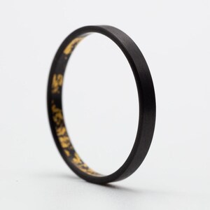 Peut inclure: Une bague noire avec une inscription dorée autour de la bande.