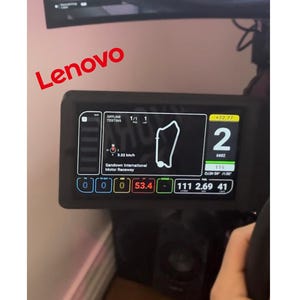 May include: A black racing simulator screen displays a digital race track map with the text "OFFLINE TESTING 1/1 1" and "Sandown International Motor Raceway". The screen also shows the number "2" with the text "+72.77", "6862", and "115". The screen also shows the numbers "0 0 0 53.4 111 2.69 41".