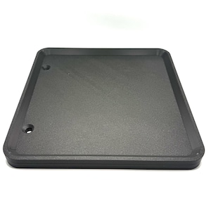 May include: A black square-shaped plastic tray with a smooth surface and rounded edges. The tray has two small holes on one side.