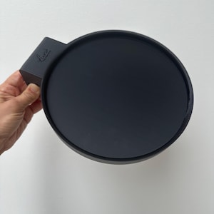 May include: Black round silicone tray with a handle. The handle has the word "Luci" printed on it.