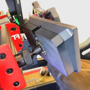 May include: A black monitor with a red and black mounting bracket. The monitor is attached to a red metal arm with a black knob. The monitor is angled towards the right.