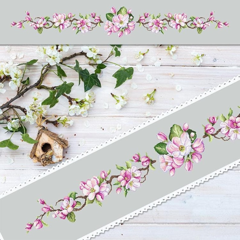 May include: A delicate floral embroidery design featuring pink blossoms and green leaves on a gray background. The design is framed by a white lace border.