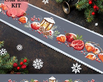 Könnte beinhalten: Ein Kreuzstich-Set mit einem grauen Tischläufer mit festlichem Design. Der Läufer ist mit Granatäpfeln, Äpfeln, einer Laterne und Tannenzapfen verziert. Der Text "Cross stitch KIT" ist sichtbar. Weiße Schneeflocken und Grünzeug vervollständigen das Weihnachtsthema.