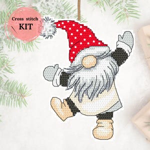 May include: Cross stitch kit with a gnome design. The gnome has a red hat with white spots, a long white beard, and a cream-coloured outfit. The kit includes the text "Cross stitch KIT" in a pink circle.