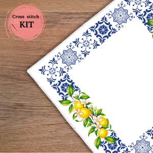 Puede incluir: Un kit de punto de cruz blanco con un diseño de borde geométrico azul. El diseño incluye un motivo de limón y flores. El texto "Cross stitch KIT" está en un círculo rosa en la esquina superior izquierda. El kit está sobre una superficie de madera.