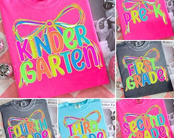 May include: A collection of colorful t-shirts with grade level text. The shirts are in various colors, including pink, gray, and blue. Each shirt features a bow design and the words "Kindergarten", "Pre-K", "First Grade", "Fourth Grade", "Third Grade", and "Second Grade".