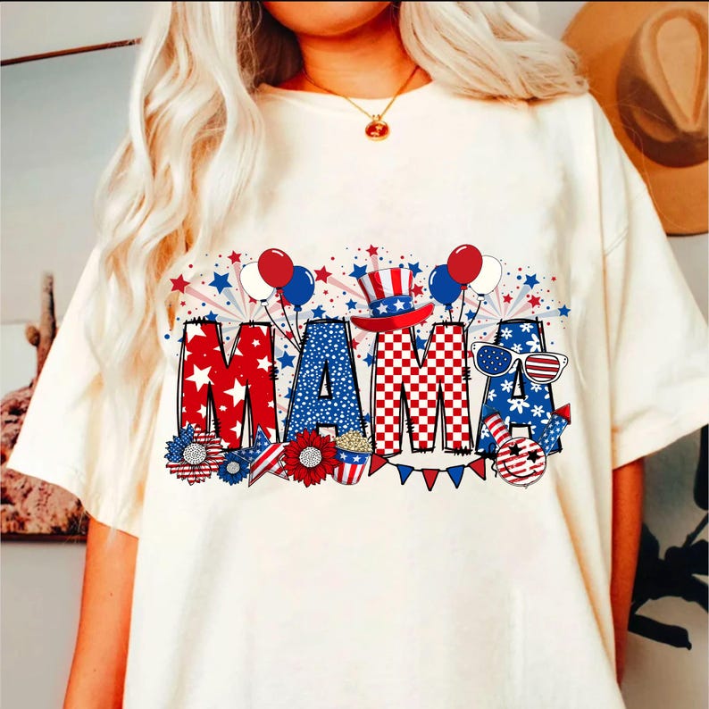 May include: White t-shirt with a red, white, and blue graphic that says "MAMA" with stars, fireworks, and balloons.