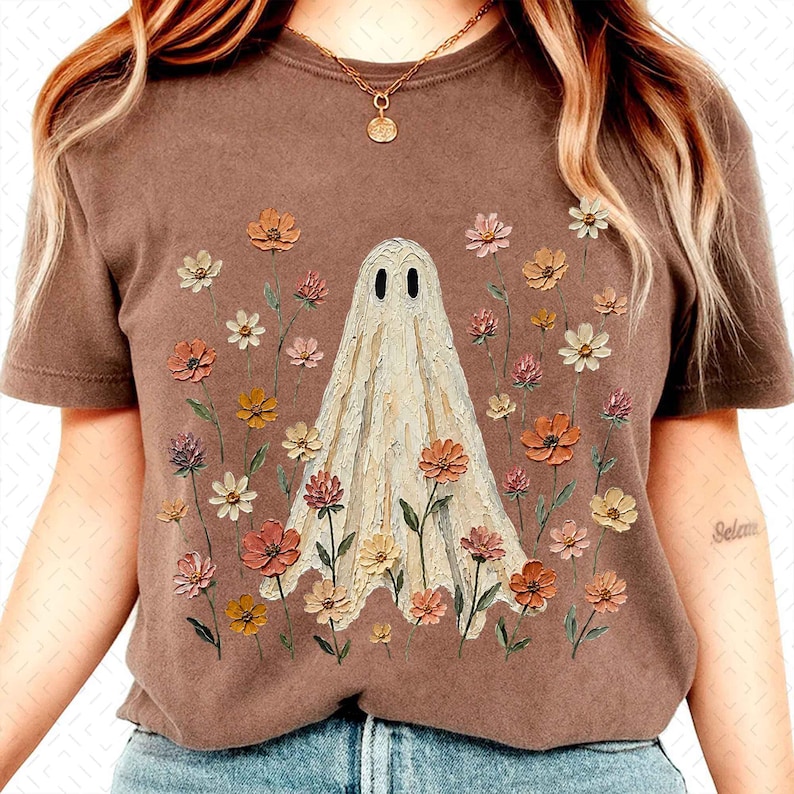 May include: A brown short-sleeve t-shirt featuring a central graphic of a white ghost surrounded by a variety of colorful wildflowers in shades of orange, pink, yellow, and white. The ghost has two black oval eyes and a textured appearance.