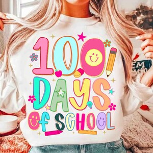 May include: White sweatshirt featuring a vibrant graphic that says "100 Days of School." The design incorporates the numbers 100, the words "Days of School," and school-related images such as a pencil, apple, and smiley faces.
